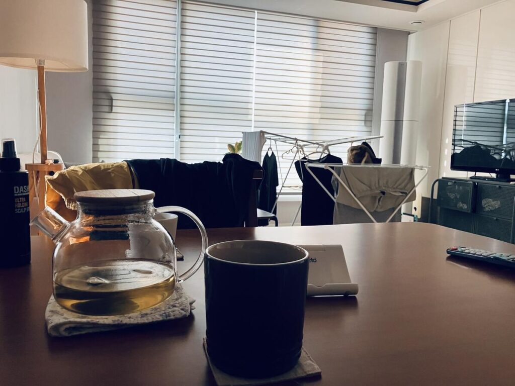 ガラスのポットと湯飲みが置かれたテーブルと、洗濯物のある室内風景