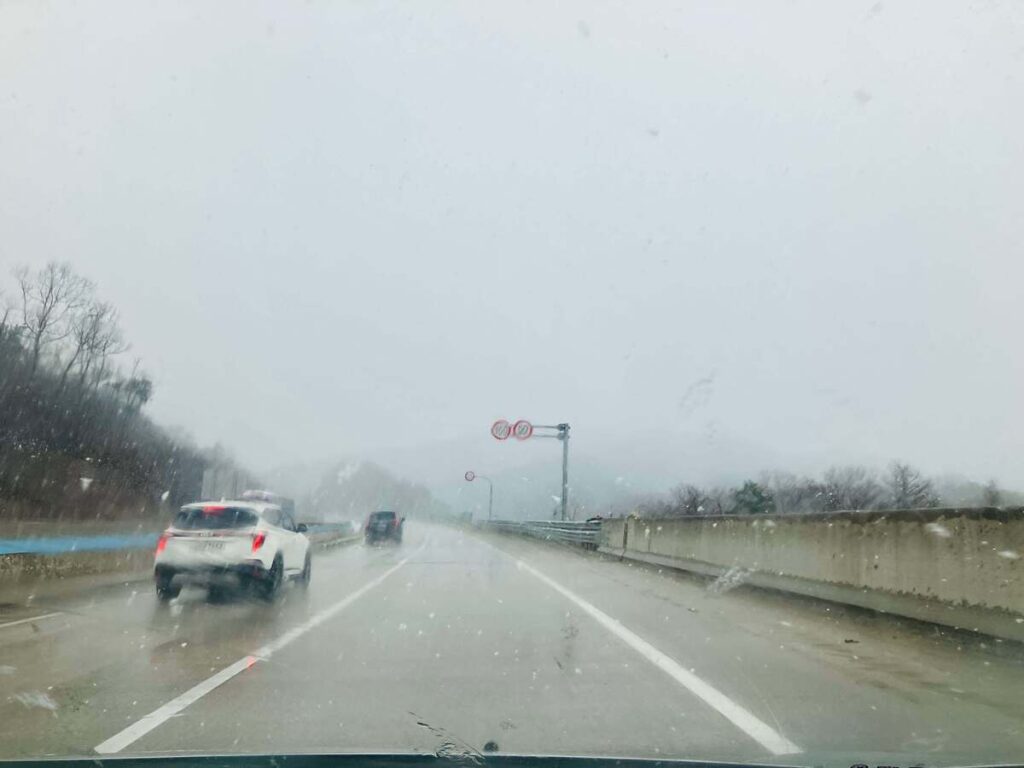 春の雪が降る中、車で山へ向かう高速道路の風景