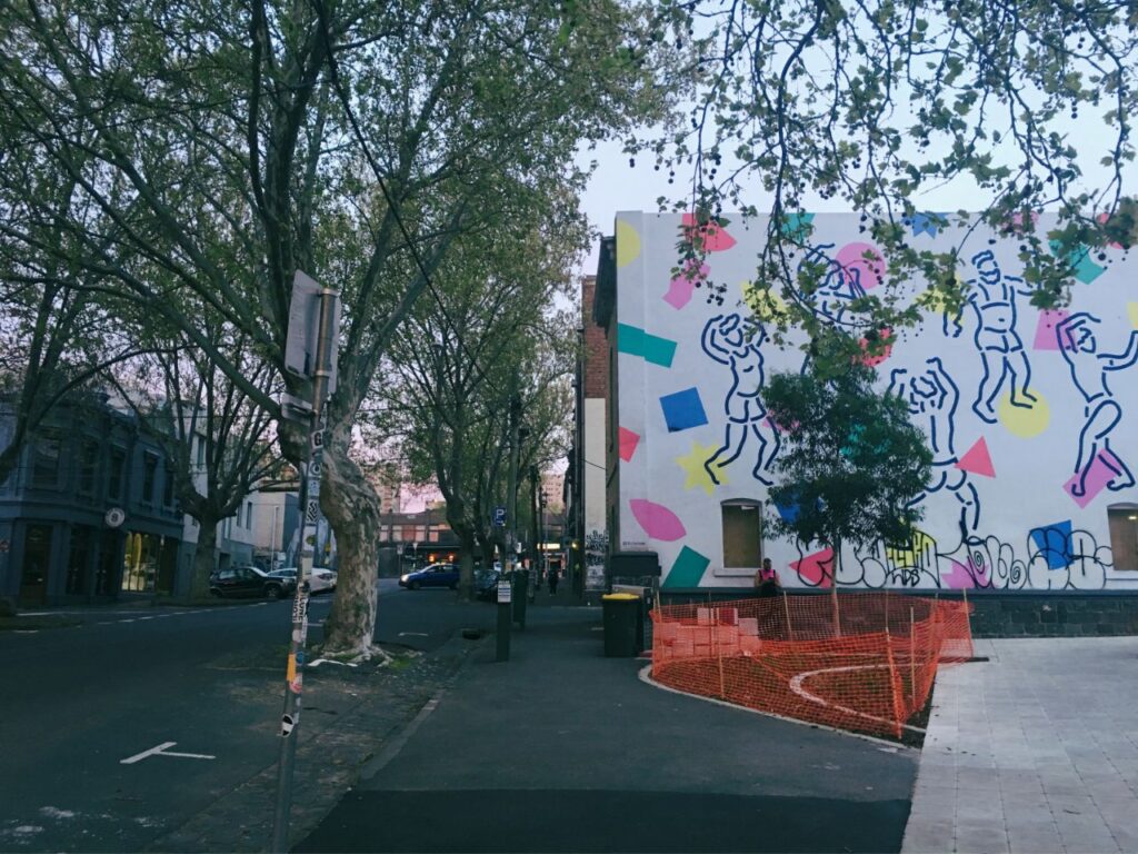 木々に囲まれた街角とカラフルな壁画｜散歩の途中で思考を整理する時間をイメージした街の風景